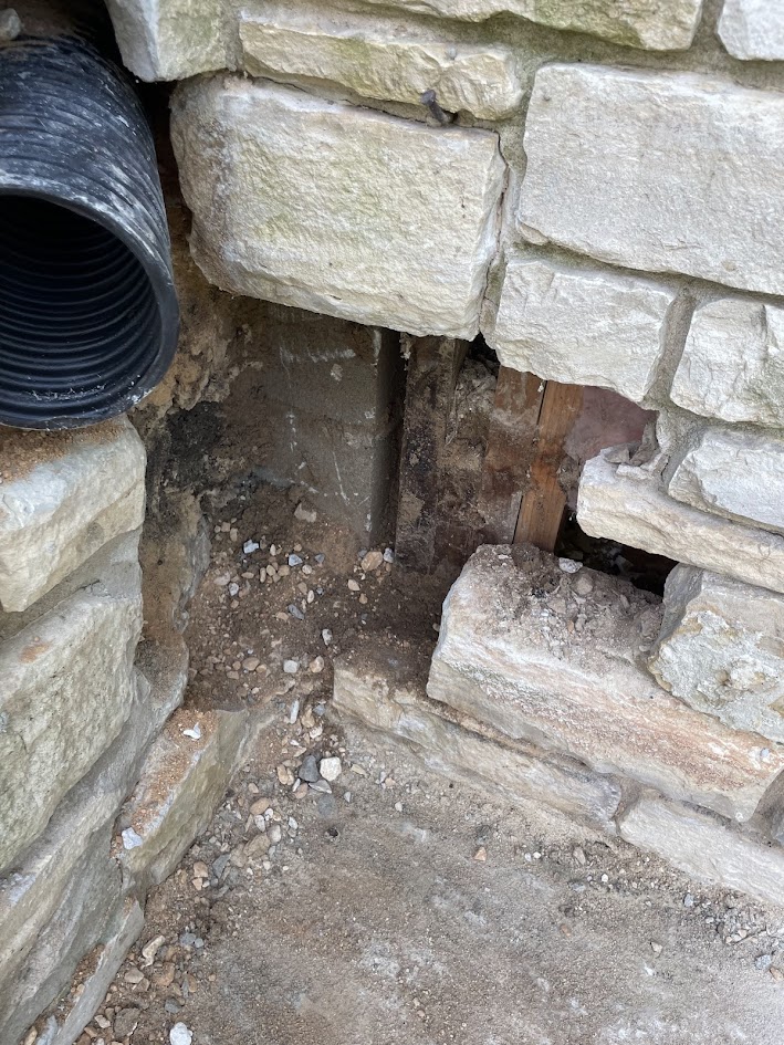 A large void in a stone wall near a drainage pipe, a structural failure that serves as a pest entry point