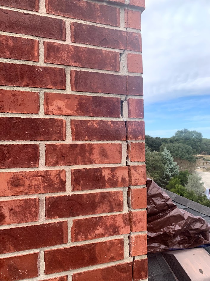 Vertical crack running through the corner of a brick chimney indicating structural movement or settlement